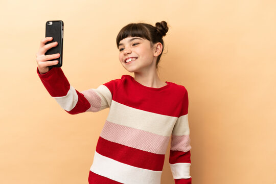 Little caucasian girl isolated on beige background making a selfie