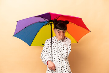 Little girl holding an umbrella isolated on beige background with tired and sick expression