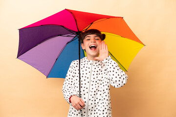Little girl holding an umbrella isolated on beige background shouting with mouth wide open