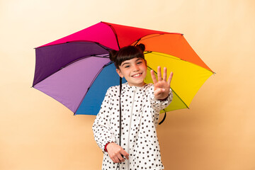 Little girl holding an umbrella isolated on beige background happy and counting four with fingers