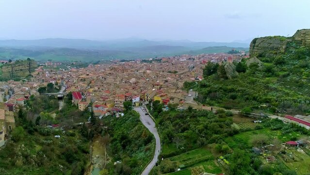 Tilt up shot of Chiesa Maria SS del Malpasso on Corleone Town, Italy on a cloudy day. Silhouette of mountain range in background. Beauitful town along the slope.