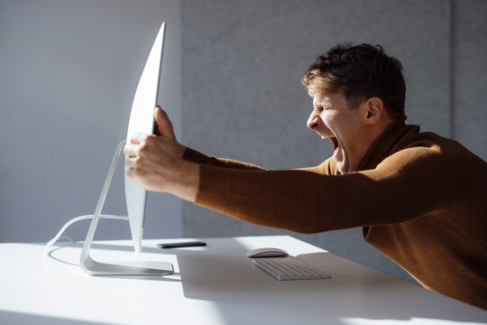 Businessman Holding Computer Monitor Screaming At Desk In Office