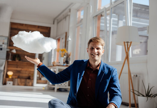 Happy businessman with levitating cloud network sitting in office
