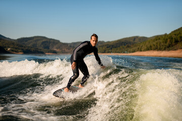 man in black wetsuit rides on splashing river wave on a wakesurf