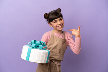 Pastry little girl holding a big cake isolated on purple background giving a thumbs up gesture