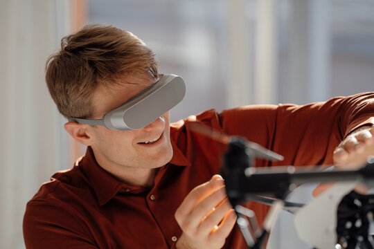 Smiling businessman wearing virtual reality simulator gesturing towards drone in office