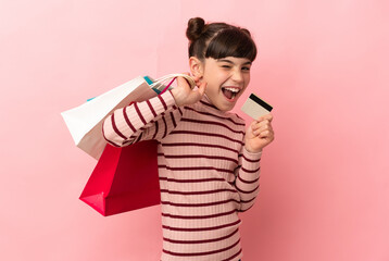 Little caucasian girl isolated on pink background holding shopping bags and a credit card