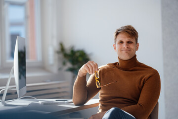 Smiling businessman holding eyeglasses sitting at desk in office