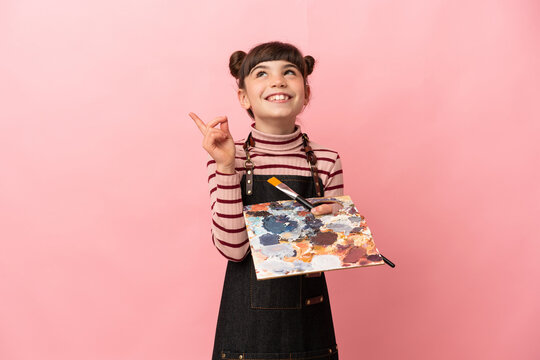 Little artist girl holding a palette isolated on pink background pointing up a great idea