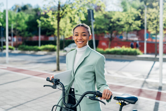 Smiling businesswoman with electric bicycle on footpath