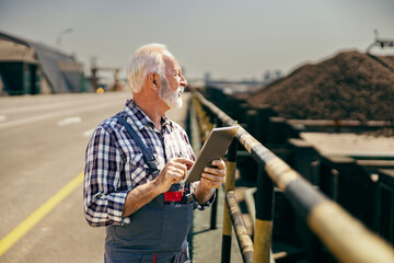 A senior worker is standing on the highway with a tablet in his hands and checking on works.