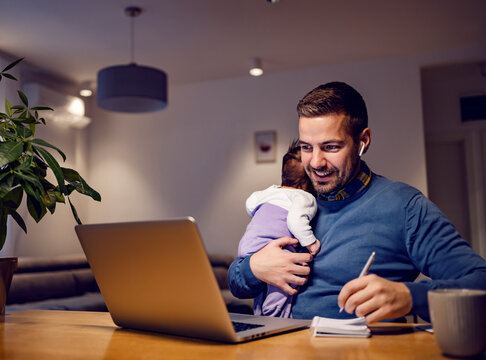 A happy entrepreneur working from home online job and holding daughter in his arms.