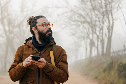Mature man wearing eyeglasses holding smart phone lost in forest