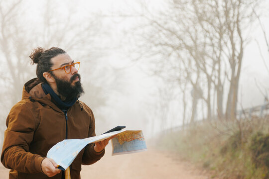 Mature bearded man wearing eyeglasses standing with map in forest