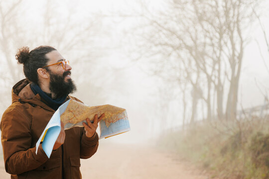 Happy bearded man with map standing in forest