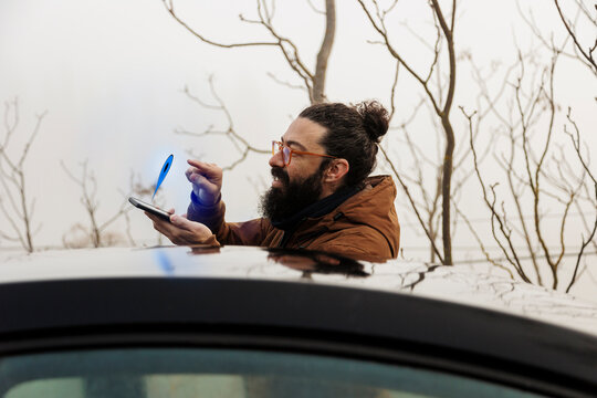 Smiling bearded man touching navigation icon on smart phone standing by car
