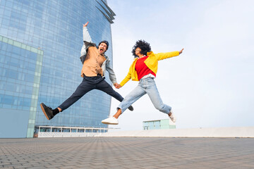 Cheerful couple holding hands jumping in front of building
