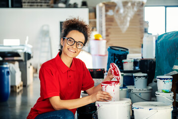 A printing shop worker kneeling next to paint buckets and smiling at the camera. © Dusan Petkovic
