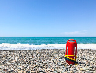 Red rescue float on rocky beach with sea panorama and no lifeguard. Static blank space copypaste background safety concept