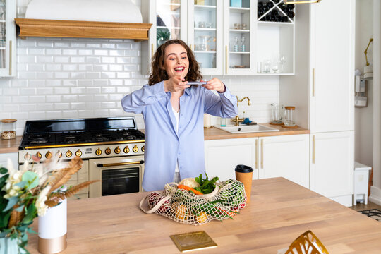 Happy woman taking picture of grocery bag in kitchen at home