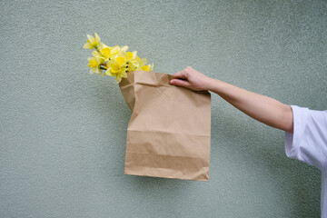 Yellow daffodils in a craft bag in the hands of a girl. The florist put together a bouquet. Beautiful spring flowers. Gift for Easter holiday. Fresh flowers for mood