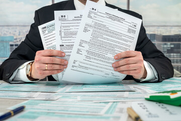 man wear black suit filling 1040 tax form and using calculator