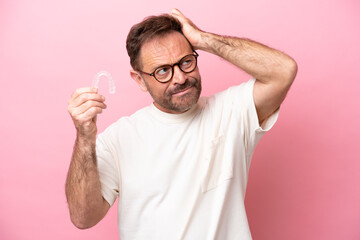 Middle age man holding invisible braces isolated on pink background having doubts and with confuse face expression