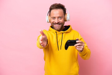 Middle age man playing with a video game controller isolated on pink background shaking hands for...