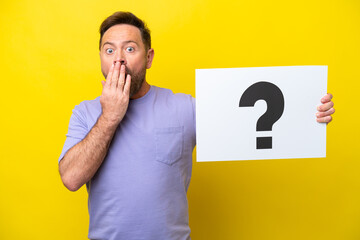 Middle age caucasian man isolated on yellow background holding a placard with question mark symbol...