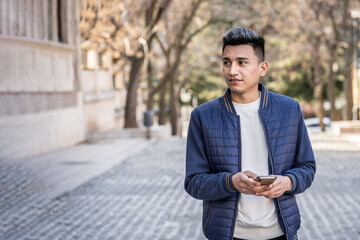 Obraz premium A young man standing on the street holding phone while looking away