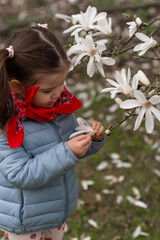 Stylish baby girl touching beautiful flowers of white Magnolia blooming.