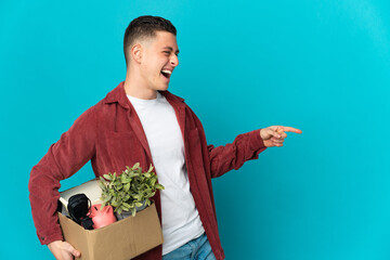Young caucasian man making a move while picking up a box full of things isolated on blue background...