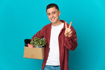 Young caucasian man making a move while picking up a box full of things isolated on blue background...
