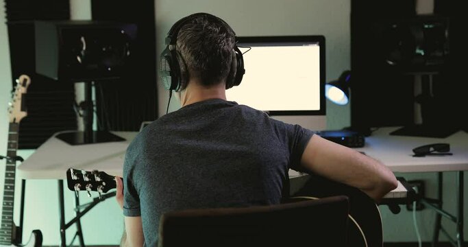 Music producer strumming some chords with the acoustic guitar while recording a new project at his home studio