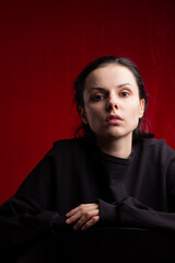 a woman in a black sweater sits at a chair, red background