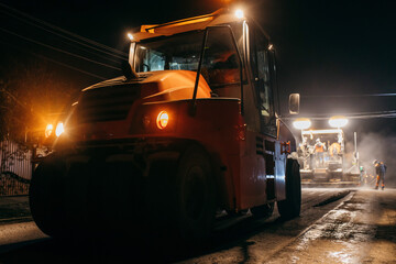 Industrial pavement truck is laying fresh asphalt on construction site at night. Road service...