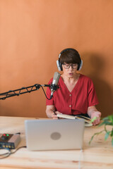 Portrait of mature woman wearing headphones and talking at online radio station - podcast and broadcast concept