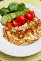 Appetizing omelet with fresh organic vegetables, tomatoes, cucumbers and lettuce leaves on a plate