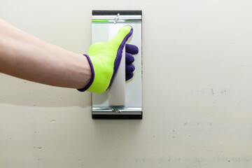 Plaster float in male hand in bright glove against a gray wall. Plastering grater in the hands of a...