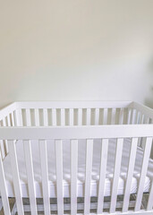 Vertical White wooden crib with white mattress in a white carpeted room