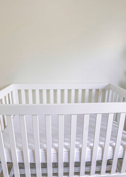 Vertical White Wooden Crib With White Mattress In A White Carpeted Room
