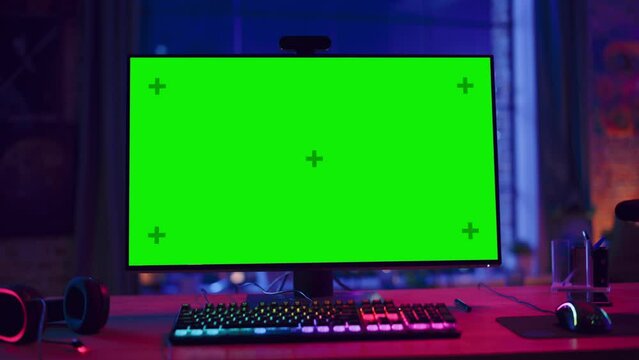 Gaming at Home: Empty Gaming Station with Player's Personal Computer with Green Screen Chroma Key Display Standing on a Wooden Desk in Stylish Loft Apartment with Neon Lights. Zoom Out Shot.