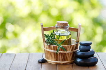 Oil bottle in basket and zen stones for hot skin massage with rosemary plant on wooden table