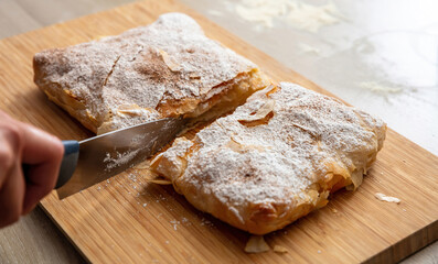 Hand with a knife and bougatsa, traditional custard pie, close up. Pastry with sugar and cinnamon.