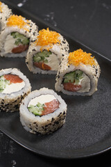 Sushi rolls in sesame with avocado and cream cheese on a black background
