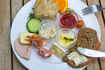 Breakfast or lunch plate with various cold cuts, whole meal bred, jam and fruits on a wooden table...