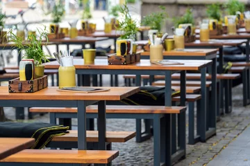 Rolgordijnen Wooden benches and set tables in a street restaurant in the  city center, urban outdoor gastronomy, selected focus © Maren Winter