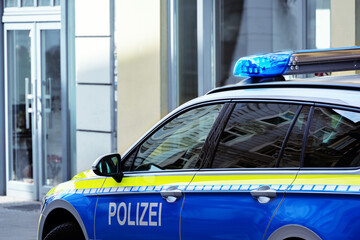 Part of a German police car (Polizei) with blue light driving in a city street, copy space,...
