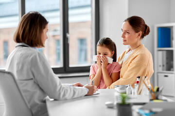 medicine, healthcare and pediatry concept - mother with little daughter blowing his nose and doctor with laptop computer at clinic