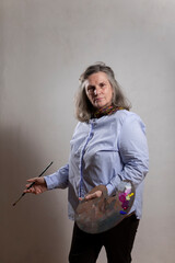 Portrait of a mature artist woman posing happy with a brush and a palette before going back to her hobby at her workshop